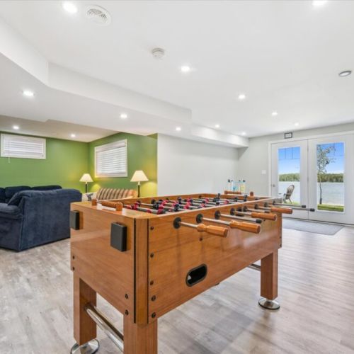 Bright lower-level rec room featuring a foosball table, cozy seating area, and walkout access to the backyard with stunning water views.