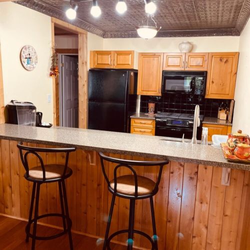 Rustic kitchen with modern lighting, wood finishes, and breakfast bar. Perfect for cozy mornings or evening wine during your cottage stay.