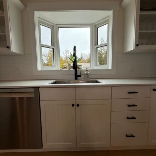 Start your mornings with a fresh coffee and a forest view from this modern bay-window kitchen—perfect for peaceful cottage living.