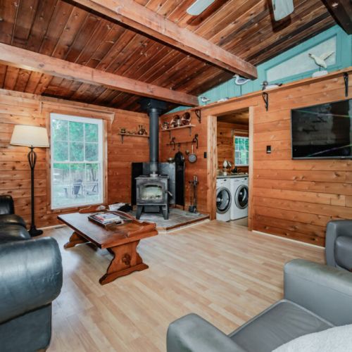 Relax in the cozy living room of this log cabin vacation rental, featuring a wood-burning stove, comfy seating, flat-screen TV, and forest views—perfect for unplugged getaways, family retreats, or romantic escapes in nature.
