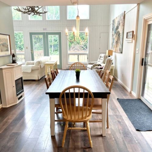 Enjoy home-cooked meals or a morning coffee at the spacious dining table, surrounded by views of the forest through large windows and sliding doors.