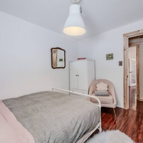 Alternate view of the guest bedroom showing cozy seating, closet space, and warm hardwood floors. Designed for comfort and ease.