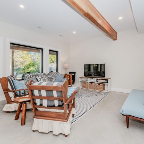 Unwind in this cozy lakeside vacation rental living room featuring rustic wood furnishings, a flatscreen TV, and large windows offering scenic views of the surrounding nature—perfect for a relaxing getaway.