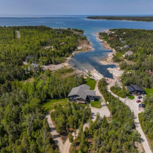 This aerial shot showcases the cottage's prime location amidst lush greenery and clear waters, offering a sense of peaceful seclusion.