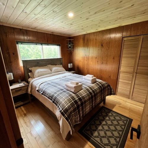 The cozy guest bedroom with a comfortable queen bed, wood-paneled walls, and a soothing natural ambiance perfect for a restful night.