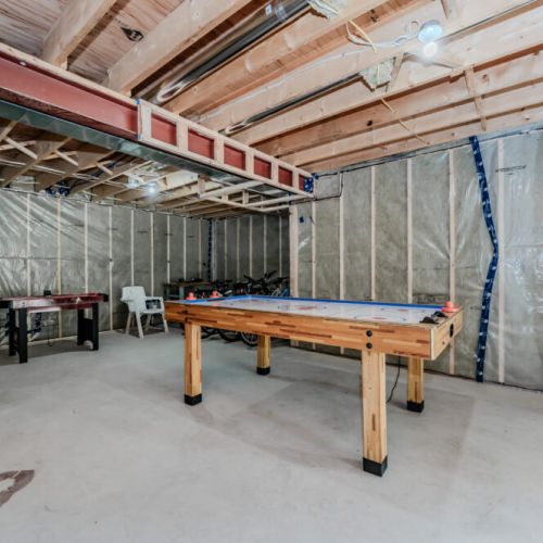 Featuring an air hockey table and additional space for activities, with the unfinished look adding a rustic charm to the area.