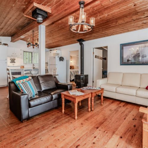Gather in the inviting living room with comfy seating, rustic wood ceiling, and a wood-burning stove—perfect for cool evenings by the lake.