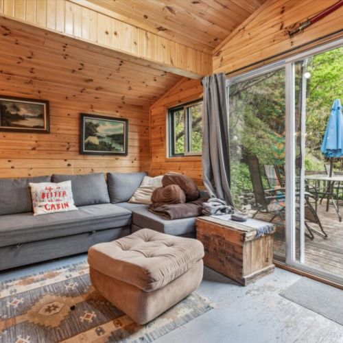 Cozy up in the second cabin’s lounge space with an L-shaped couch, vintage artwork, and easy access to the outdoor dining deck via large sliding doors. It’s the perfect spot for a morning coffee or rainy-day relaxation.