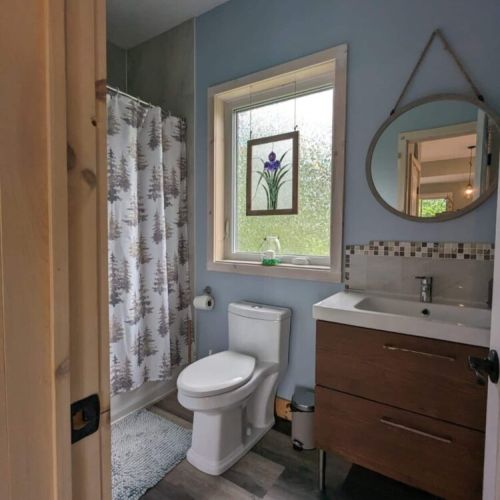 Bright, modern full bathroom with a walk-in shower, fresh towels, and thoughtful touches—including a nature-inspired stained-glass window.