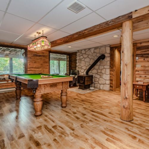 The lower-level games room offers endless entertainment with a billiard table, wood accents, and a cozy wood stove—perfect for gathering with family and friends.