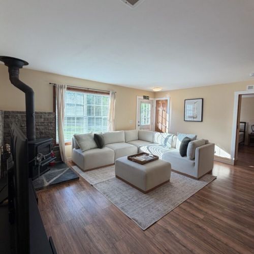 The perfect place to relax and reconnect—this airy living room offers ample seating, warm wood floors, and a cozy cottage atmosphere.
