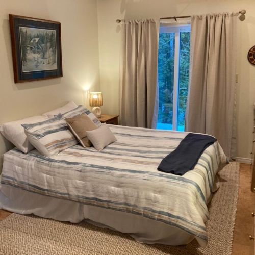 A cozy cottage bedroom with soft linens, warm lamplight, and a glass door opening to the woods.